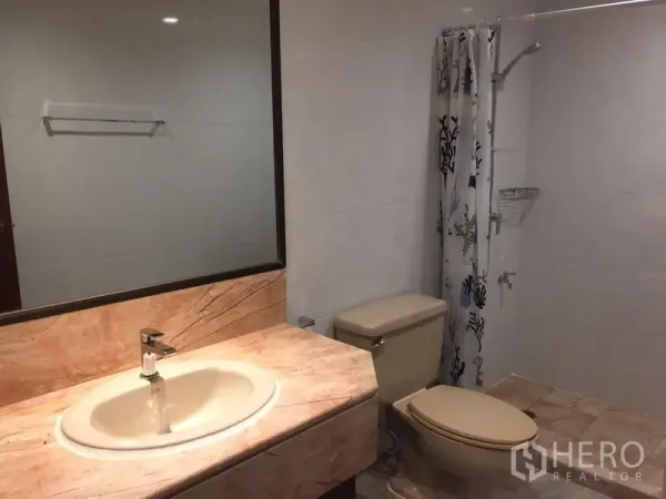 Condominium for rent in Sathon, Bangkok - Bathroom with marble-top vanity, large mirror, toilet and walk-in shower with curtain.