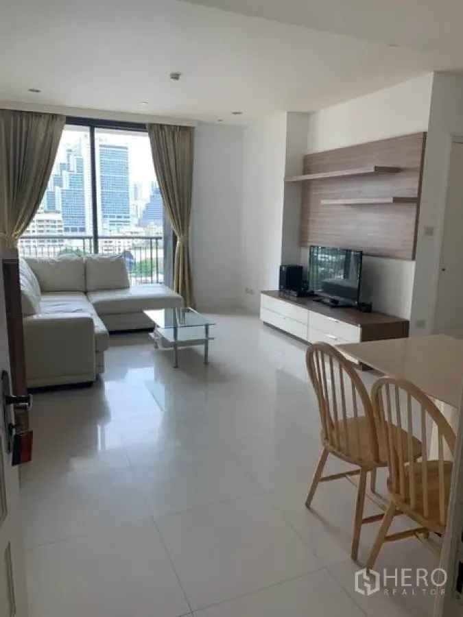Condominium for rent in Khlong Toei, Bangkok - Bright living room with L-shaped sofa, TV console and a balcony offering a city skyline view.