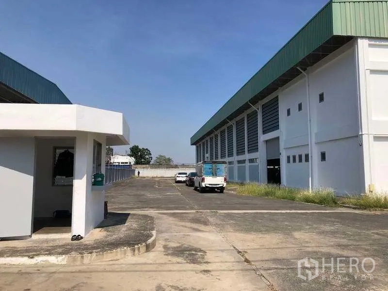 Factory for rent or sale in Phra Nakhon Si Ayutthaya - Security gatehouse and wide access road with on-site parking beside the factory building.