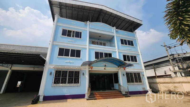 Factory for rent in Pak Kret, Nonthaburi - Front facade of the blue three-storey office with entrance canopy and parking forecourt