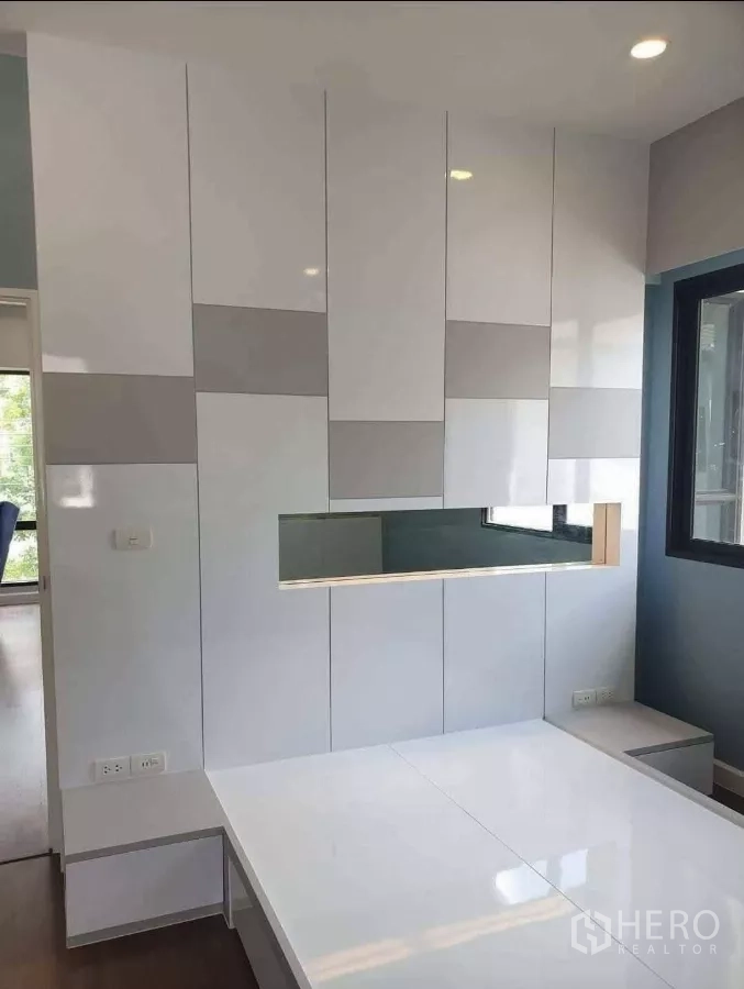 Detached House for rent or sale in Prawet, Bangkok - Bedroom with glossy white built-in cabinetry and platform bed by corner windows