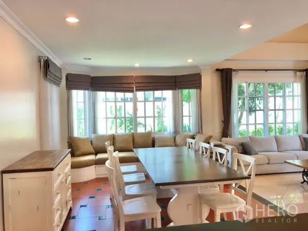 Detached House for rent in Mueang Samut Prakan, Samut Prakan - Open‑plan dining area with long table, bay‑window bench seating, recessed lighting and garden views.