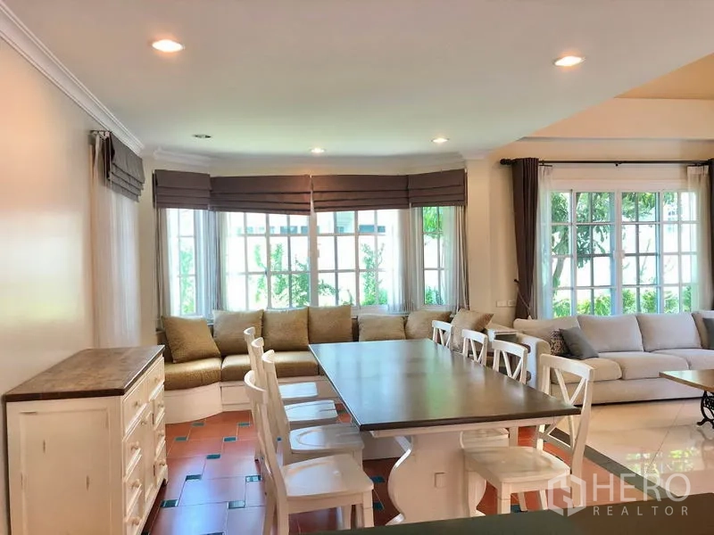 Detached House for rent in Mueang Samut Prakan, Samut Prakan - Open‑plan dining area with long table, bay‑window bench seating, recessed lighting and garden views.