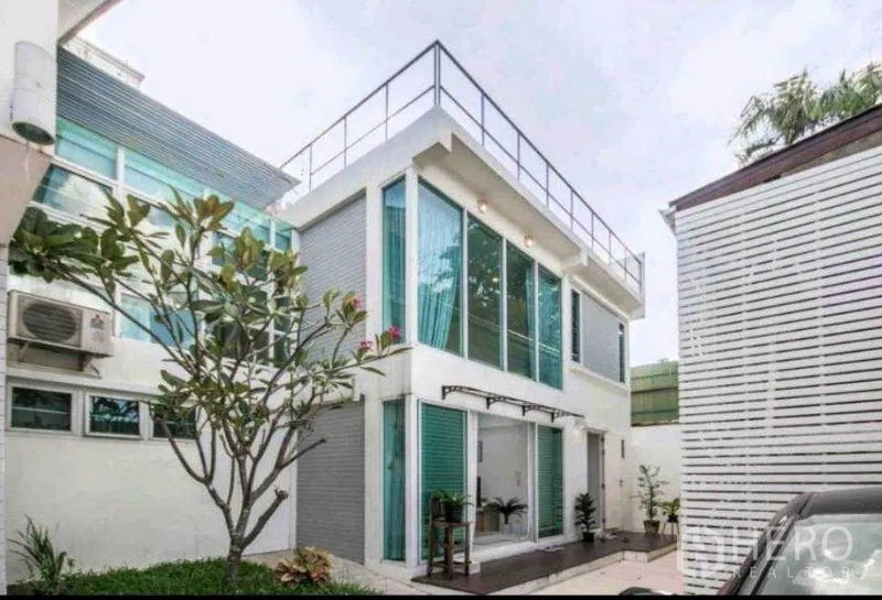 Townhouse for rent in Khlong Toei, Bangkok - Two-story townhouse exterior with blue-tinted windows and a rooftop terrace railing.