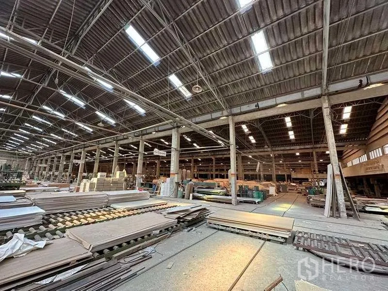 Factory for rent in Sai Noi, Nonthaburi - Production floor with materials and equipment beneath a lit steel truss roof.