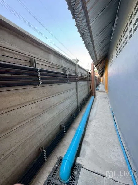 Warehouse for rent in Bang Phli, Samut Prakan - Narrow maintenance walkway with drainage and utility piping along the boundary wall