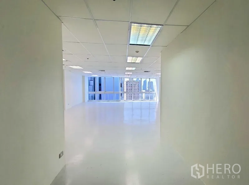 办公空间 出租在Khlong Toei, Bangkok - 明亮的入口走廊通向开放式办公区，白色地面、吊顶灯具与大窗户，可见曼谷天际线。
