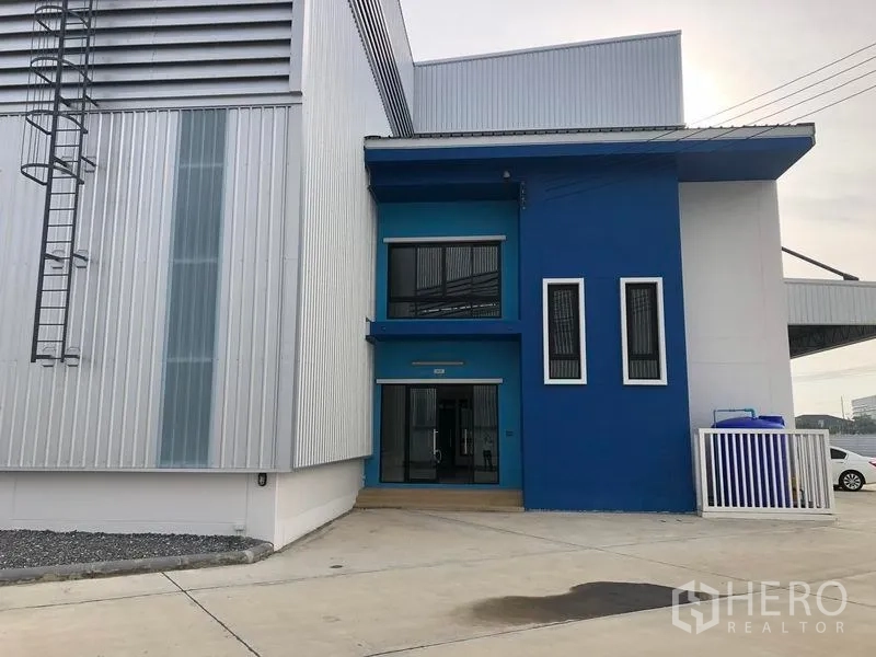 工厂 出租在Samut Prakan - 侧入口展示蓝色办公立面，与金属板厂房相连。