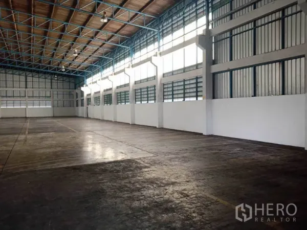 Factory for rent in Samut Prakan - Bright factory space featuring tall windows, blue steel beams and a wide column-free area.