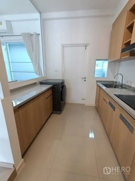 Townhouse for rent in Prawet, Bangkok - Kitchen from opposite angle showing long countertops, sink and a washing machine.