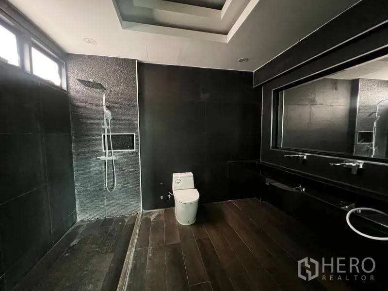 Detached House for sale in Lat Phrao, Bangkok - Contemporary dark-tiled bathroom with rain shower, long vanity, and large mirror.