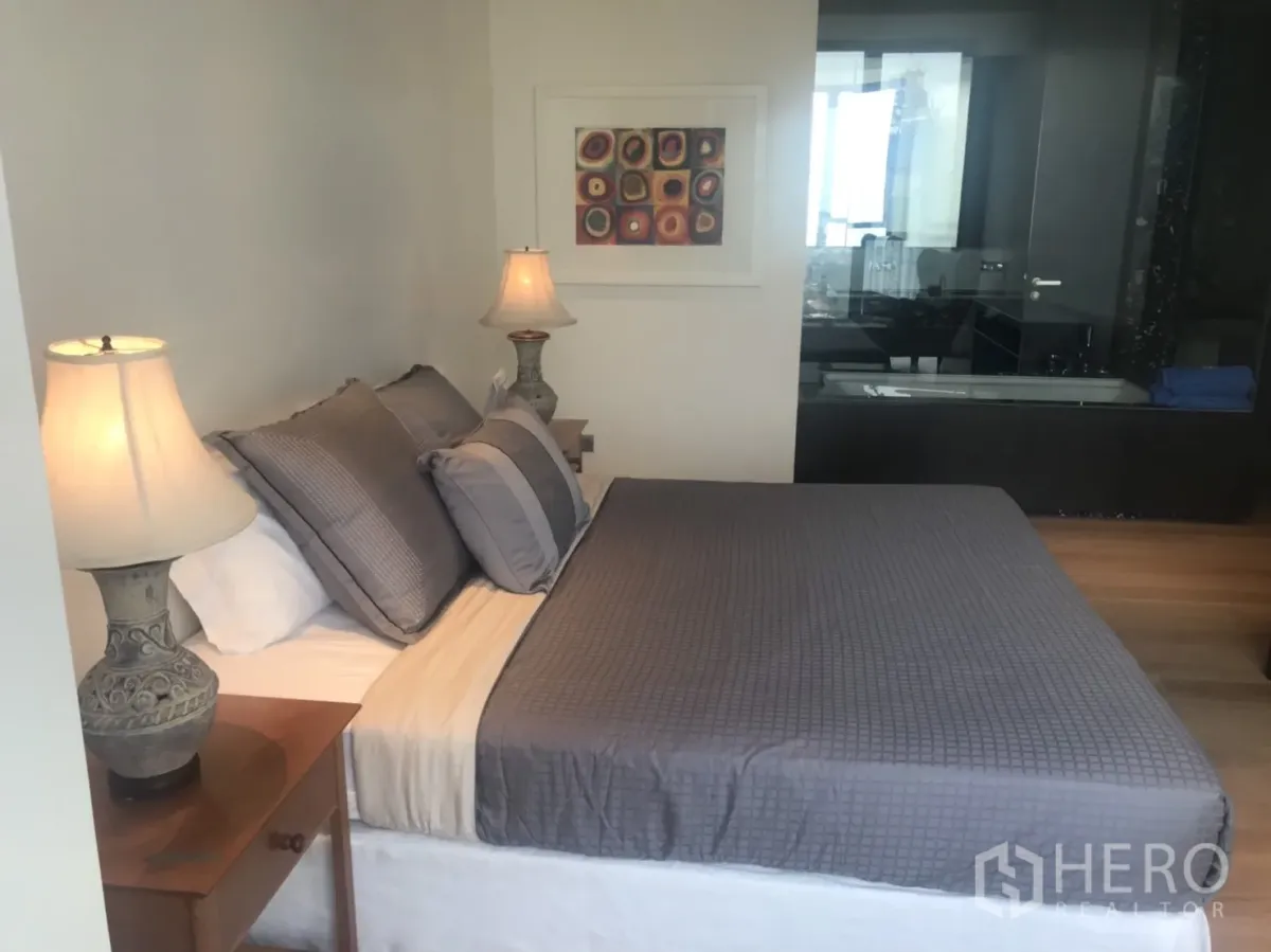 Condominium for rent or sale in Khlong Toei, Bangkok - Master bedroom with double bed, bedside lamps and a glass-walled bathroom.