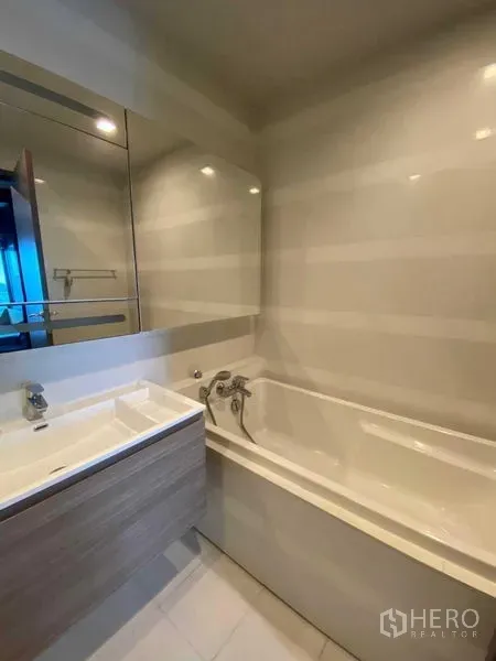 Condominium for rent in Khlong Toei, Bangkok - Bathroom with built-in bathtub, large mirror and sleek vanity.