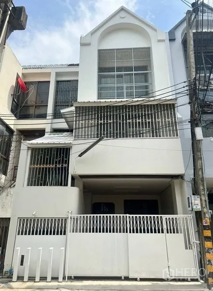 联排别墅 出售在Khlong Toei, Bangkok - 三层白色联排别墅外立面，带围栏车位、金属护栏窗和阳台，位于素坤逸一带，晴天拍摄。