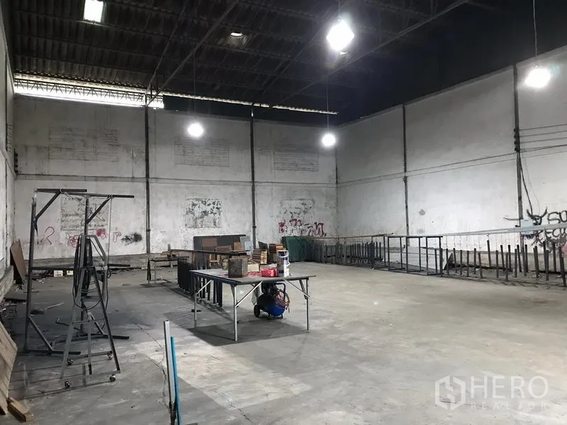 Warehouse for rent in Bang Phli, Samut Prakan - Spacious warehouse interior in Bang Phli with high steel roof, bright hanging lights, concrete floor and open storage area.