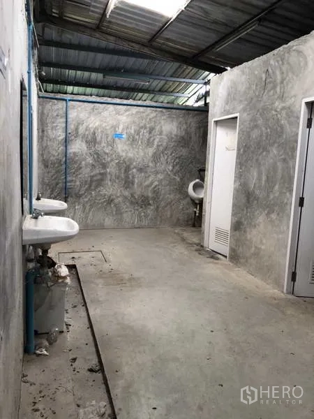 Warehouse for rent or sale in Khlong Luang, Pathum Thani - Utility washroom with wall-mounted sinks and toilet doors in a concrete finish.
