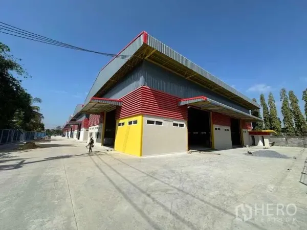 Warehouse for rent in Lam Luk Ka, Pathum Thani - Corner view of the warehouse block with covered loading docks, broad concrete forecourt, and a tree-lined boundary.