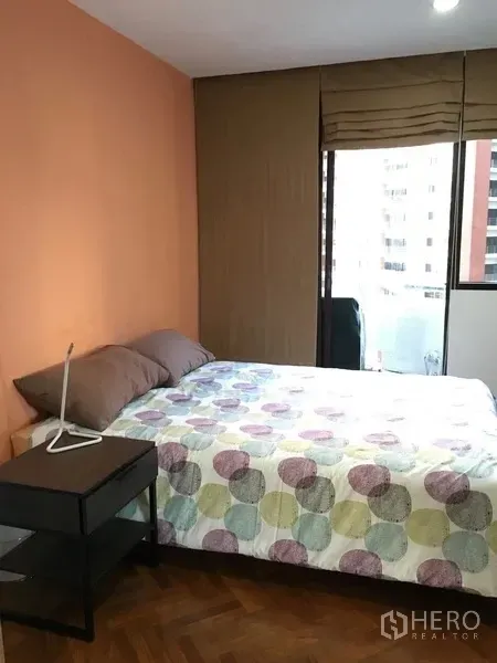 Condominium for rent in Pathum Wan, Bangkok - Second bedroom with orange feature wall, double bed, bedside table, and city-facing window with blinds.