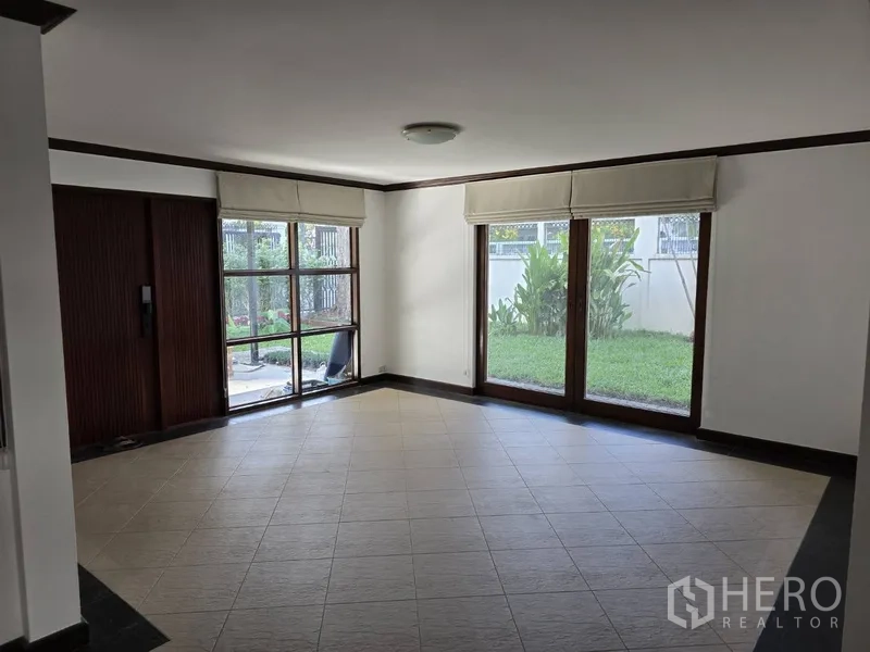 Detached House for rent in Watthana, Bangkok - Bright living room with floor tiles and large garden-view sliding windows.