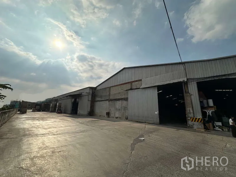 Warehouse for rent in Mueang Pathum Thani, Pathum Thani - Metal-clad warehouse exterior with wide concrete yard under a bright sky.