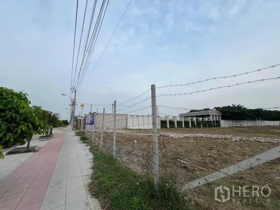 地 出租在Lat Krabang, Bangkok - 街道侧视图，带铁丝网围栏的土地，设人行道与电线杆，周边低层建筑。