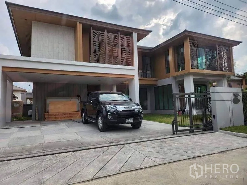 独立式住宅 出售在Sai Mai, Bangkok - 两层独栋别墅正立面，带木质格栅、入户电动门与双车位车棚。