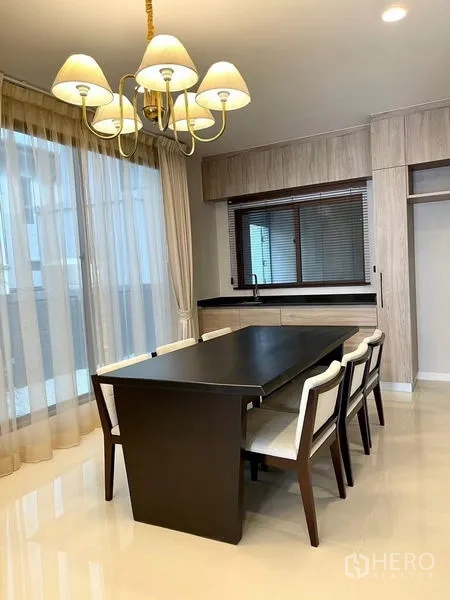 Detached House for sale in Bang Kapi, Bangkok - Dining area with dark wood table, four upholstered chairs, chandelier and built-in cabinetry beside a window.