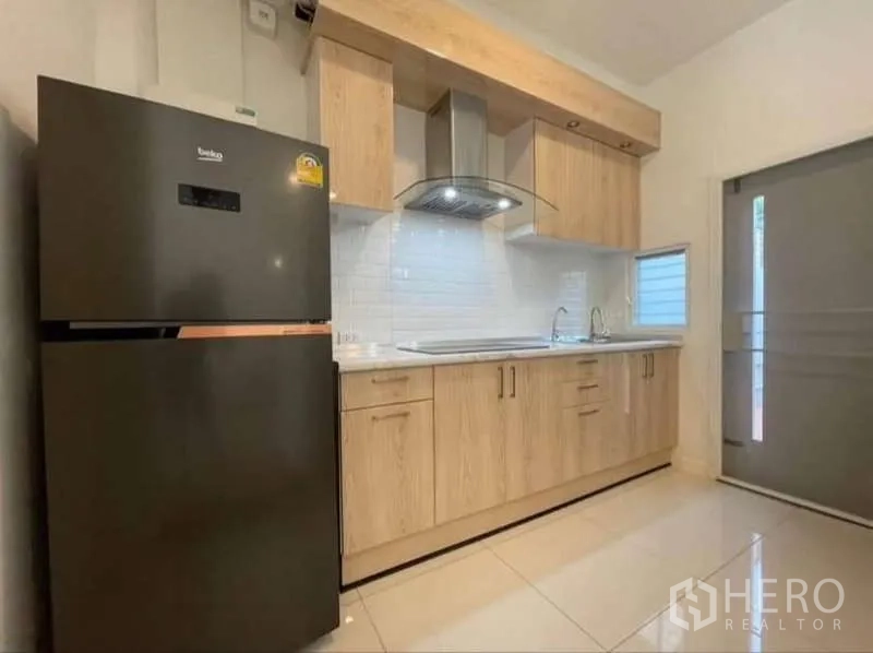 Townhouse for rent in Prawet, Bangkok - Kitchen with fridge, range hood, and wood cabinets against white tiles