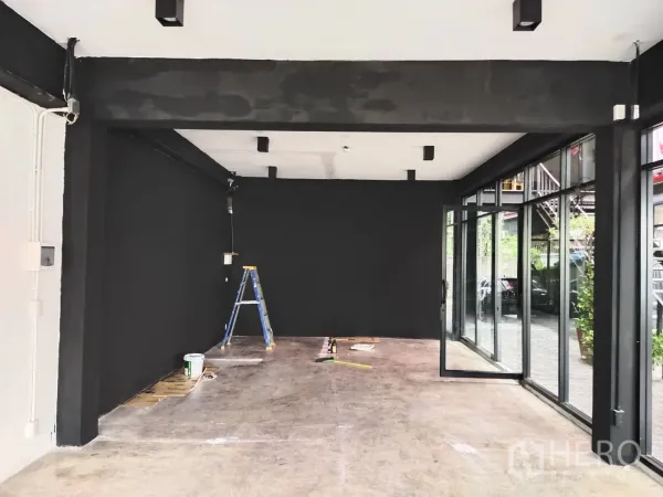 Retail Space for rent - Retail space with black feature wall, ceiling lights and corner glass doors opening to a courtyard, mid-renovation.