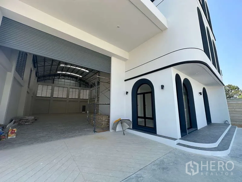 Factory for sale in Lam Luk Ka, Pathum Thani - Loading area and office entrance beside the oversized rolling shutter of the warehouse.