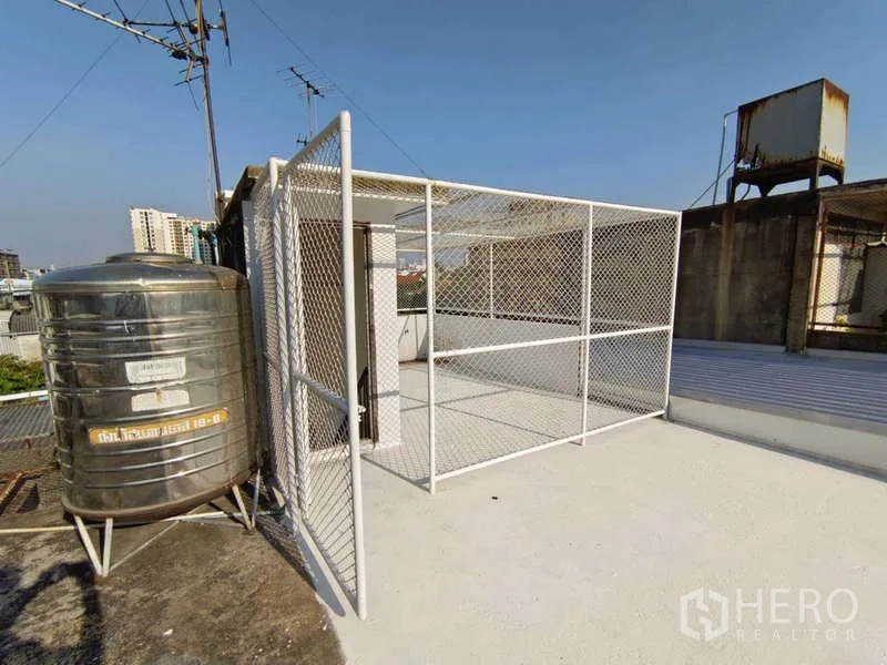 Shophouse for rent in Bang Na, Bangkok - Rooftop terrace with water tank and caged utility area.