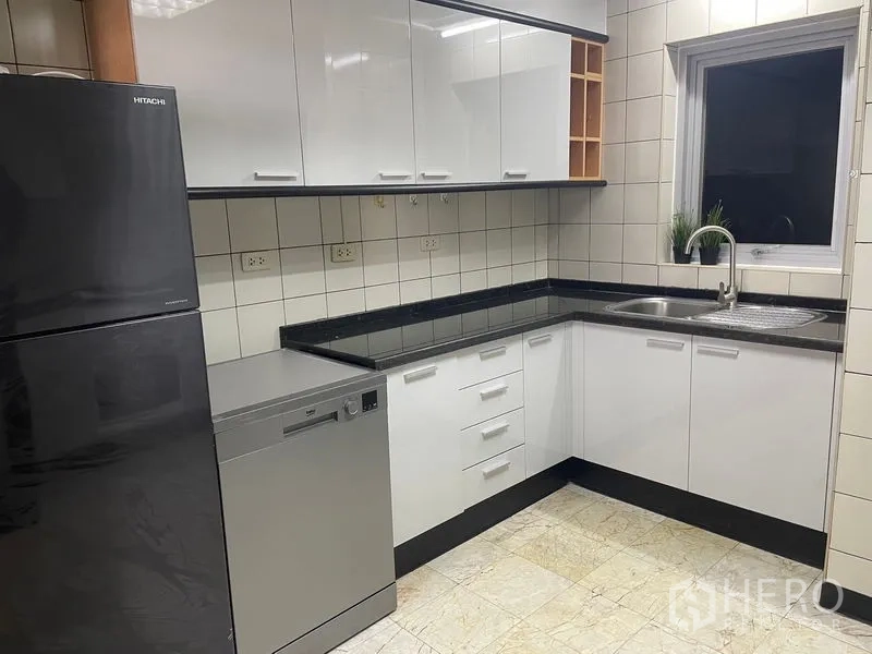 Condominium for rent in Pathum Wan, Bangkok - U-shaped kitchen featuring white cabinetry, black countertops, sink and dishwasher.