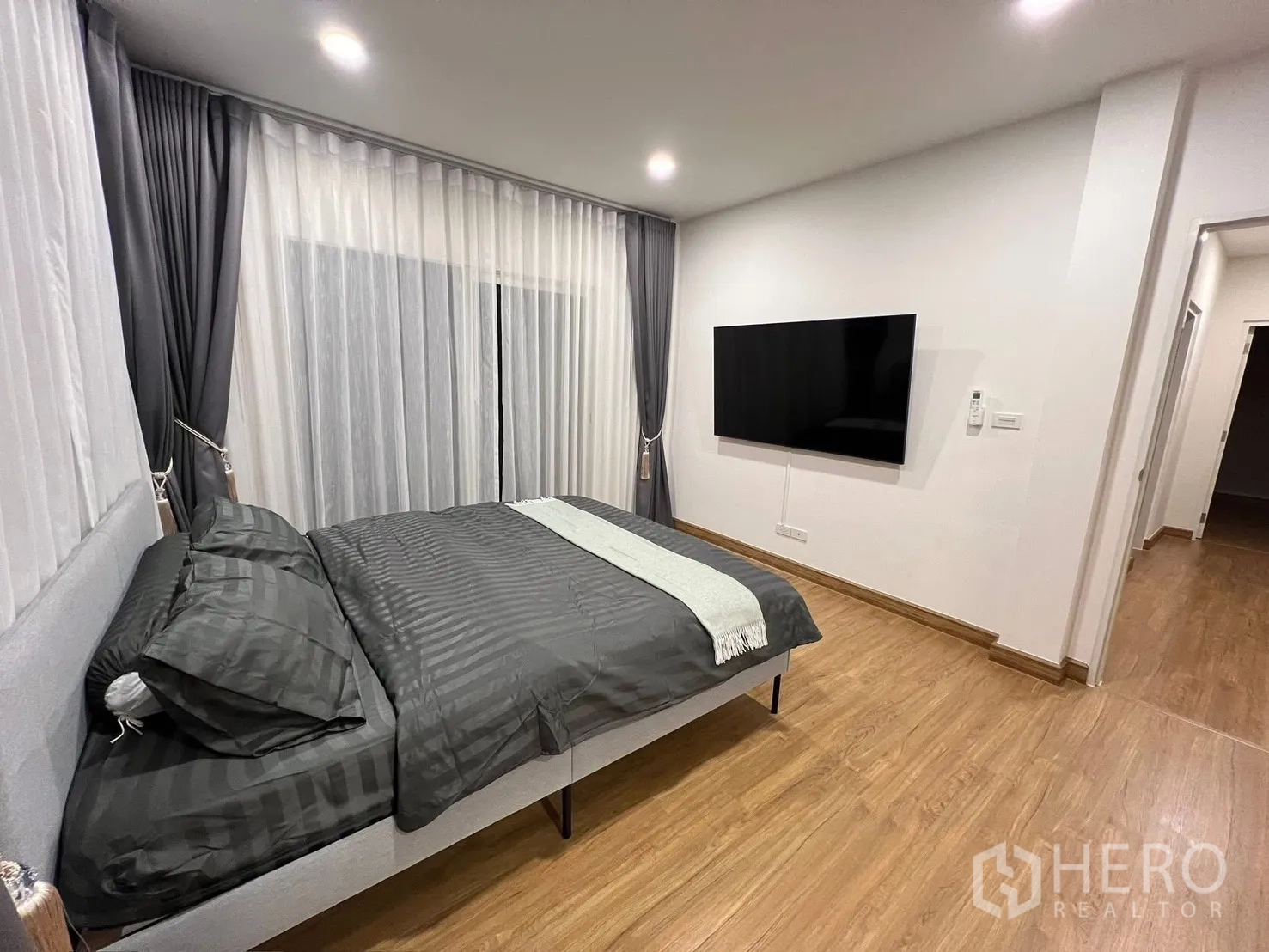 Detached House for rent in Prawet, Bangkok - Master bedroom with wall-mounted TV opposite the bed and floor-to-ceiling curtains.