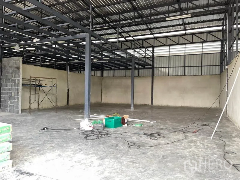 Warehouse for rent in Pathum Thani - Bright interior showing steel beam grid, scaffold and smooth concrete floor.