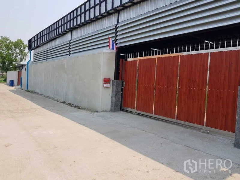 Warehouse for sale in Lam Luk Ka, Pathum Thani - Front elevation of the warehouse with wood-look sliding gate along a quiet access lane.