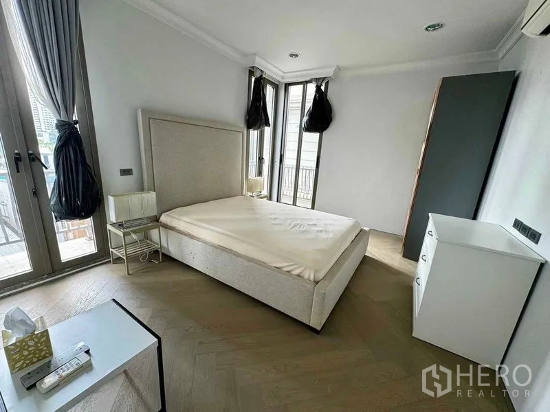 Townhouse for rent in Watthana, Bangkok - Bright bedroom with corner windows, balcony doors and minimalist furniture.