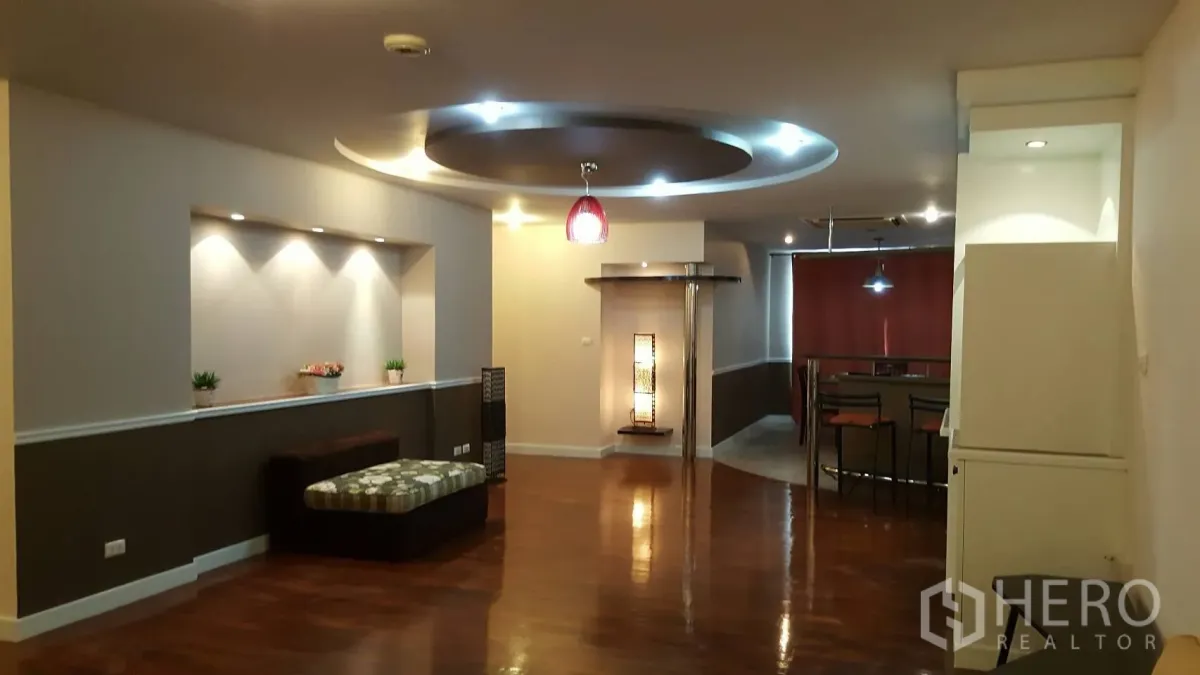 Condominium for rent in Khlong Toei, Bangkok - Spacious living area with polished wood floors, recessed wall niche and circular ceiling lighting leading to the dining zone.