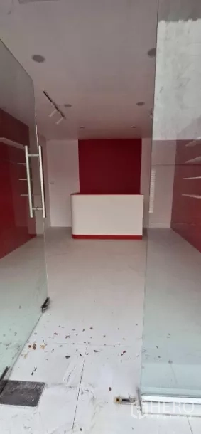 Retail Space for rent in Watthana, Bangkok - View through full-height glass doors into a red-and-white shop space with counter and shelving.
