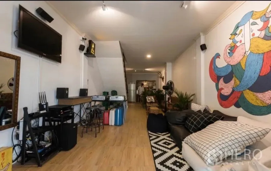 Townhouse for rent in Khlong Toei, Bangkok - Open-plan living room with wood floors, large mural feature wall, TV and sofa in a Khlong Toei townhouse.