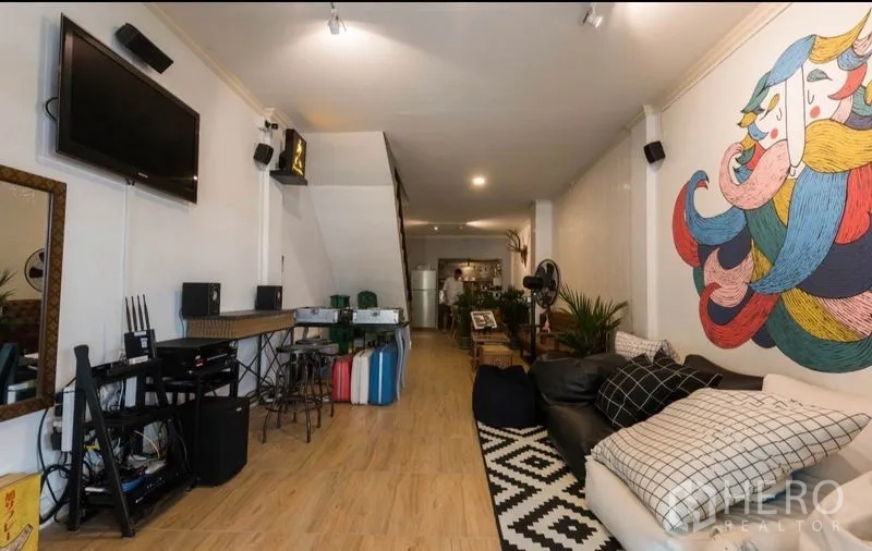 Townhouse for rent in Khlong Toei, Bangkok - Open-plan living room with wood floors, large mural feature wall, TV and sofa in a Khlong Toei townhouse.