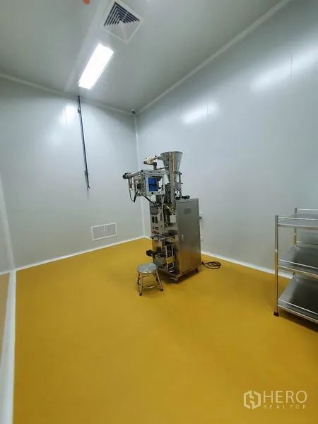 Factory for sale in Lam Luk Ka, Pathum Thani - Production room housing a small packing machine on a yellow epoxy floor with ventilation grille.