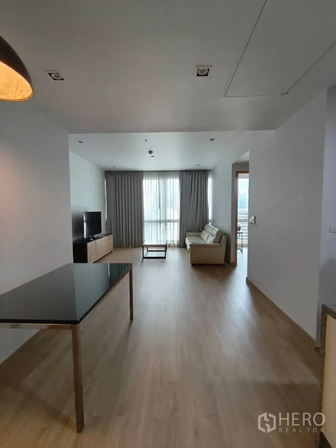 Condominium for rent in Khlong Toei, Bangkok - Open-plan living and dining area with light wood floors, sofa, TV console, and floor-to-ceiling window allowing city light.
