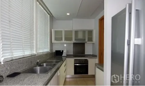 Condominium for rent in Khlong Toei, Bangkok - Modern galley kitchen with granite countertops, double sink, built-in oven and cooktop, and a large refrigerator.