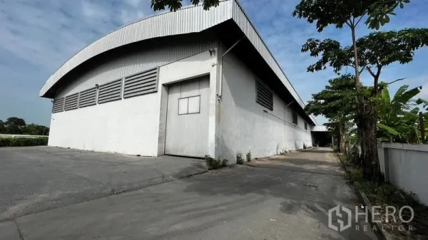 Factory for rent or sale in Pathum Thani - Large white factory with curved metal roof and wide driveway in Lam Luk Ka.