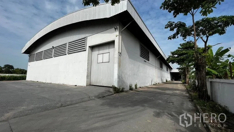 Factory for rent or sale in Pathum Thani - Large white factory with curved metal roof and wide driveway in Lam Luk Ka.