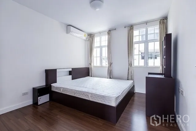联排别墅 出租在Watthana, Bangkok - 卧室配深色木床、空调与双层窗户，自然采光充足。