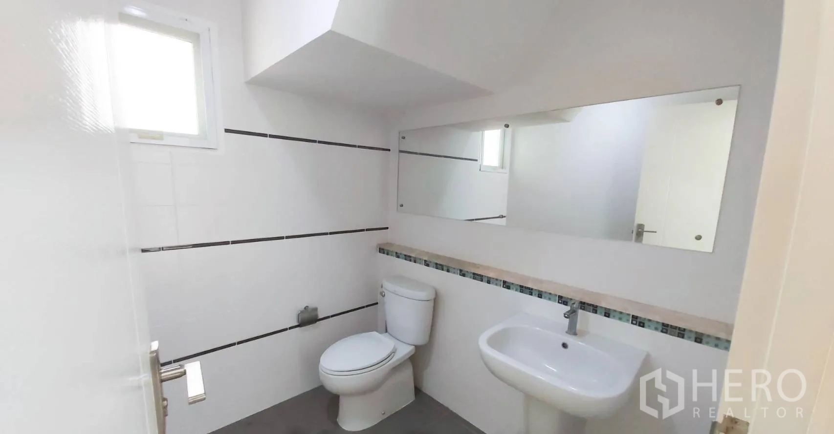 Detached House for sale in Bang Kapi, Bangkok - Clean white bathroom with toilet, sink and an oversized wall mirror.