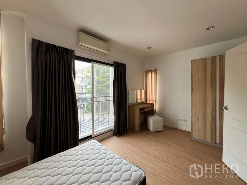 联排别墅 出租在Bang Kapi, Bangkok - 明亮卧室，推拉阳台门、书妆台与衣柜，木地板。
