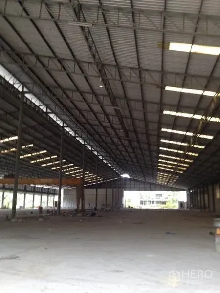 Warehouse for rent in Mueang Chon Buri, Chon Buri - Expansive warehouse interior with high steel truss roof, skylight panels, and open concrete floor.