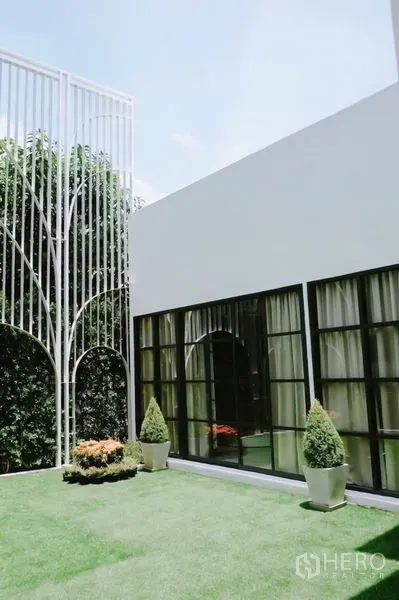 บ้าน ให้เช่าในHuai Khwang, Bangkok - บ้านเดี่ยวสีขาวสไตล์โมเดิร์น หน้าต่างกรอบดำ เปิดสู่สนามหญ้าและซุ้มเหล็กตกแต่ง
